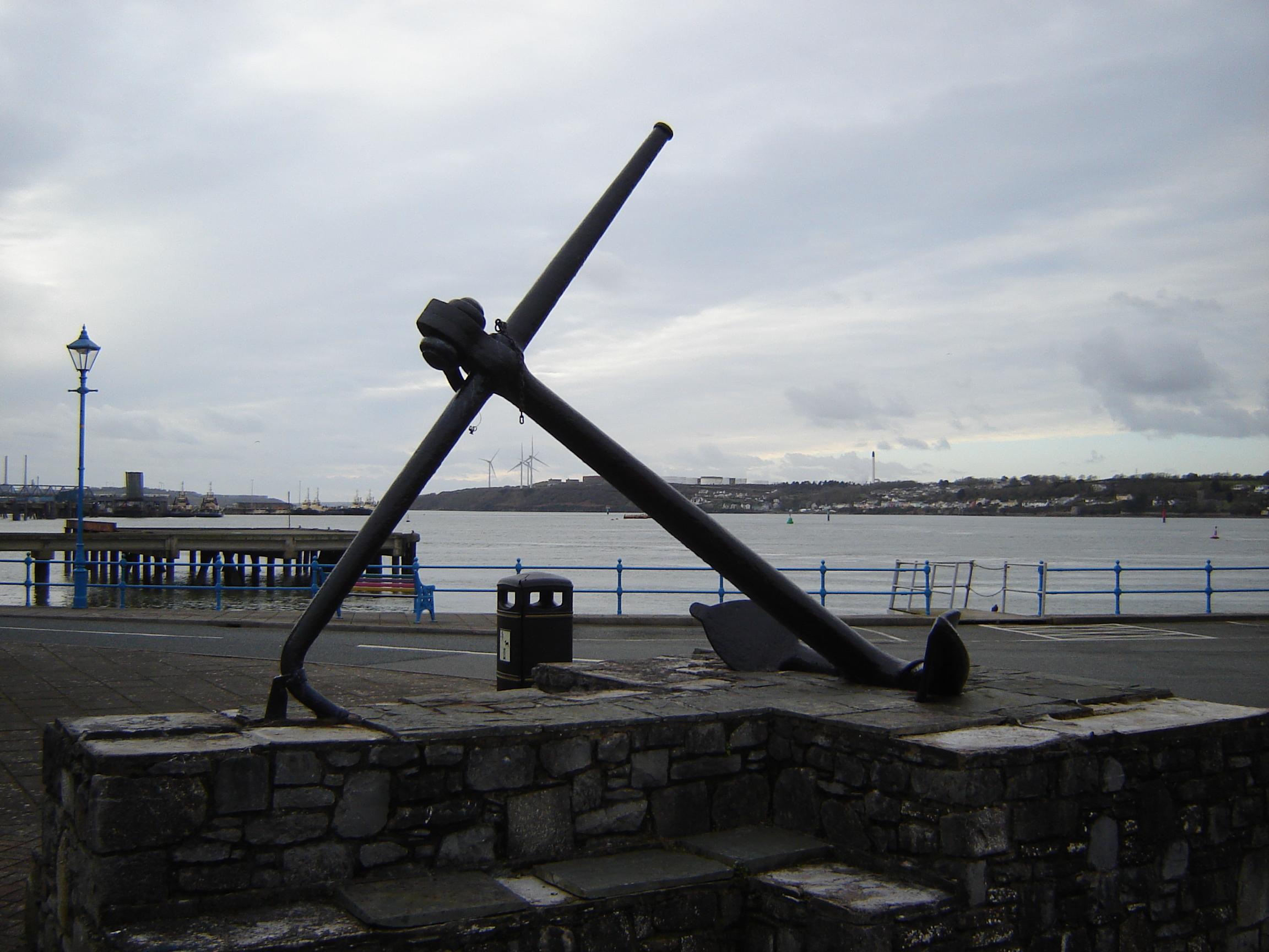 An anchor outside the Pembroke Haven Yacht Club at the eastern end of Milford Haven, with a 21st century wind farm in the background.